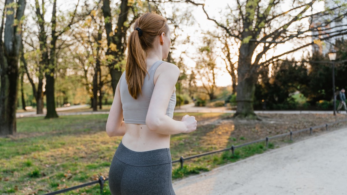 A woman jogs in a park during sunset, enjoying an outdoor fitness routine.
