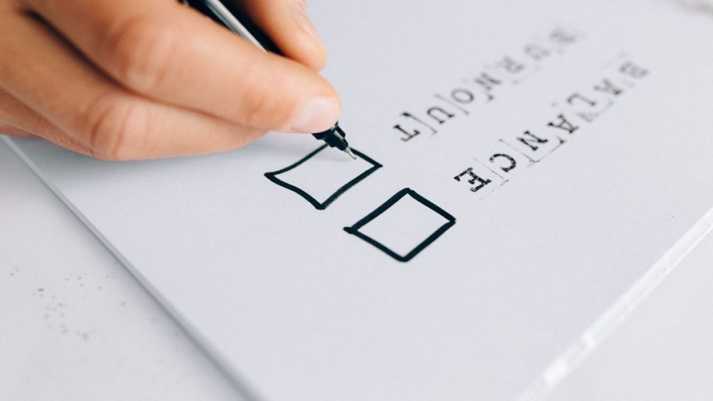 A hand drawing checkboxes on a checklist, themed around balance and burnout.