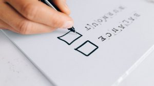 A hand drawing checkboxes on a checklist, themed around balance and burnout.